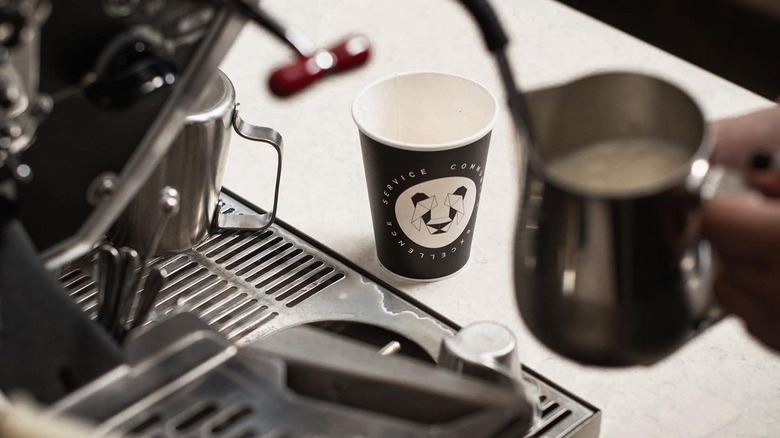 A Black & White Coffee Roasters cup sits on a counter as a barista steams milk