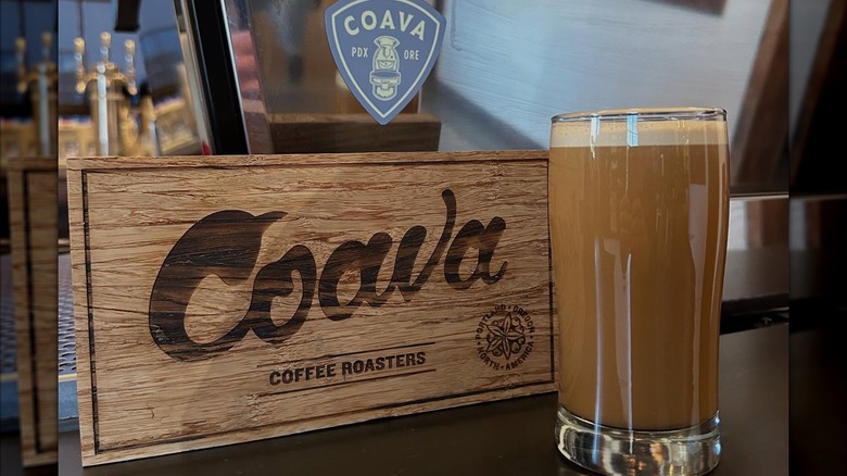 Coffee beverage in a tall glass next to a wood-burned sign that reads Coava Coffee Roasters