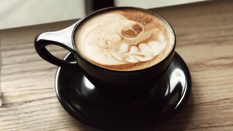 Latte in a black coffee mug sits on a wooden table