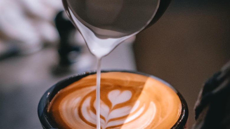 Steamed milk pours into a cup of coffee, creating latte art