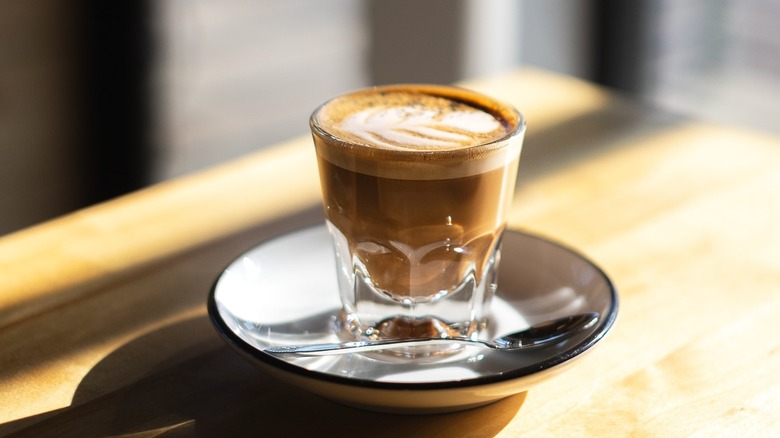 Coffee beverage in a small glass on a white saucer with a spoon