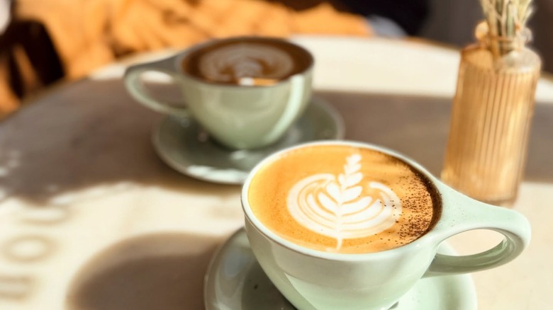 Two lattes in white mugs with white saucers on a table
