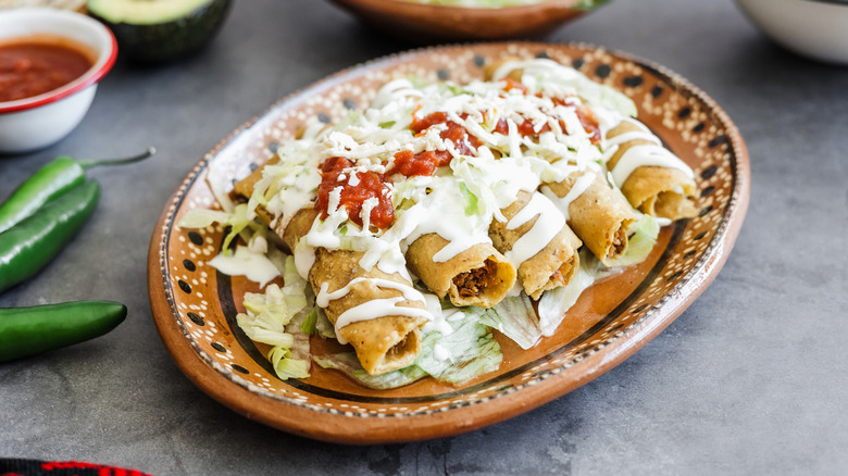 plate of flautas topped with sour cream and salsa