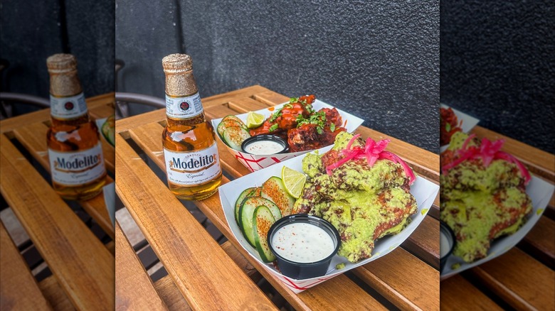 Chicken wings coated with green sauce next to beer from La Diabla Denver