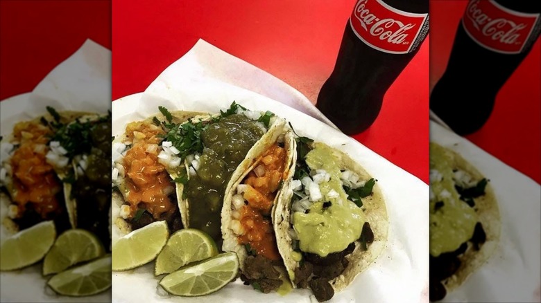 Four tacos on paper with lime slices and Coca-Cola at Carniceria y Tortilleria San Antonio
