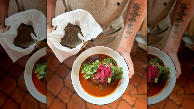 Hands presenting corn tortillas and cochinita in bowls
