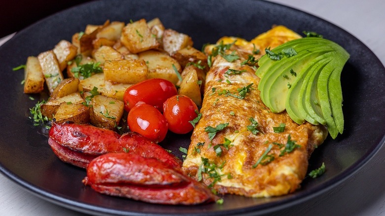 Mexican-style roasted potatoes, tomatoes, omelet, and avocado on a plate