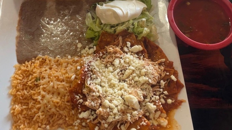 beans, rice, salsa, lettuce, sour cream, and shredded meat topped with cheese on plate at Mexican restaurant