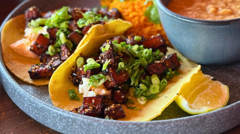 Tacos de Camote on plate with lemon wedge, bowl of refried beans, and seasoned rice