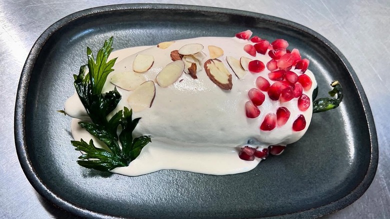 Fine dining stuffed poblano pepper topped with walnut sauce, pomegranate seeds, and sliced almonds on plate