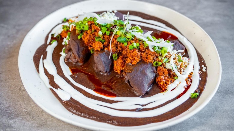 a Mexican dish in mole sauce with rings of white sauce and topped with several ingredients