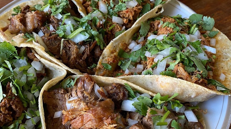 Various soft shell tacos stuffed with shredded meat and toppings on plate