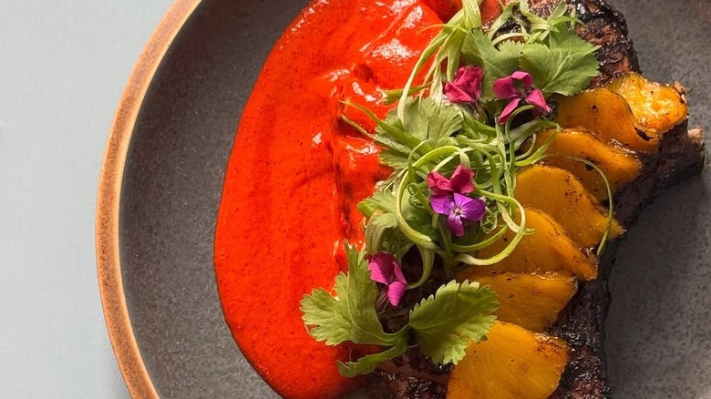 Pork Chop Al Pastor topped with pineapple, greens, and sauce arranged in fine-dining manner on plate