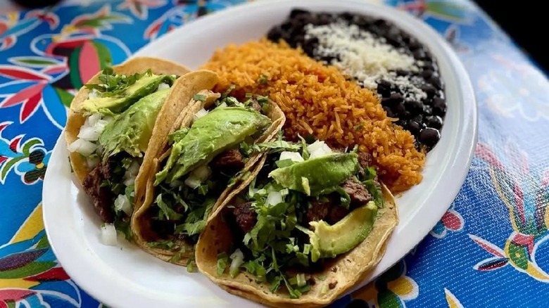 three soft tacos, beans, and rice on a plate