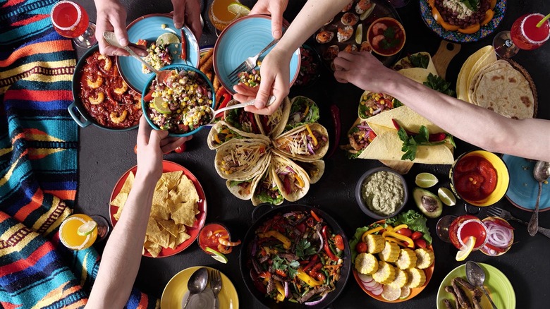 Birds eye view of a table with an assorment of Mexican food and hands grabbing food