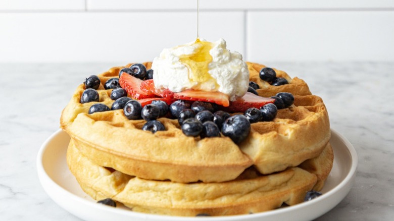 fluffy golden brown belgian waffles topped with fresh berries, whipped cream, and maple syrup