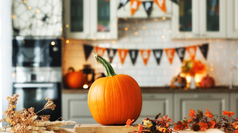 pumpkin on cutting board in kitchen with Halloween/fall decor all around
