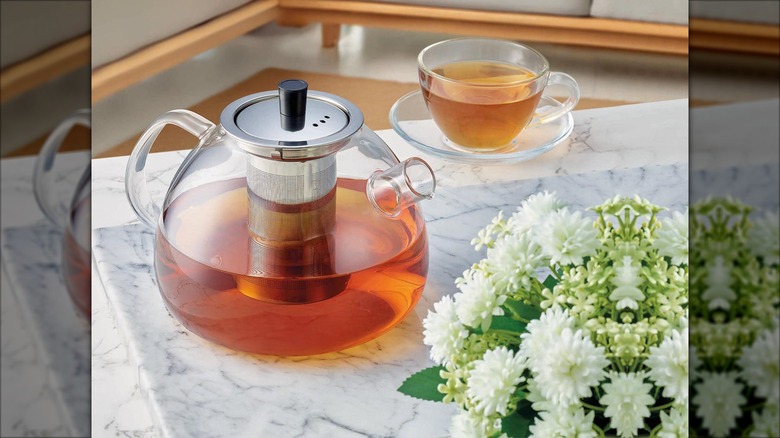 glass teapot on counter with cup and flower centerpiece