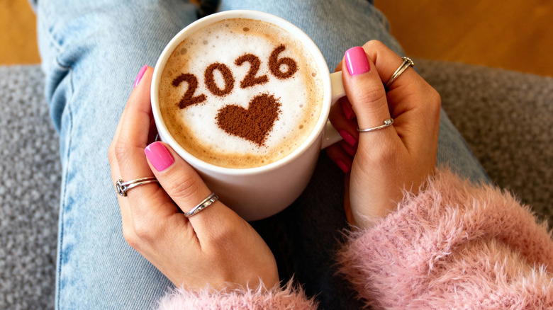 person holding cup with latte art reading 2026 plus heart