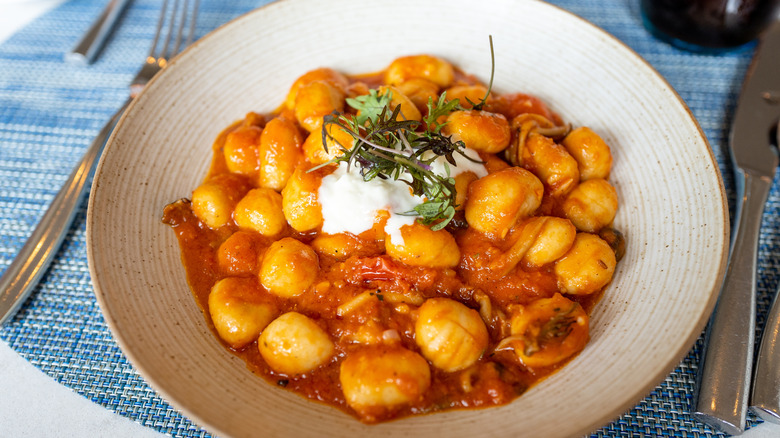 Gnocchi in red sauce with garnish in white dish on blue place mat