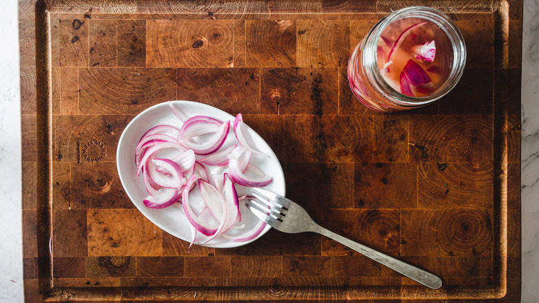 Pickled onions in a white bowl with a fork and in a nearby jar.