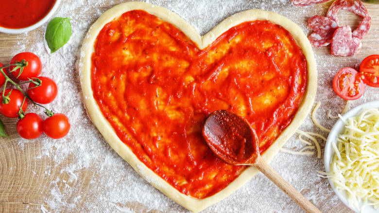 spreading sauce on heart shape pizza