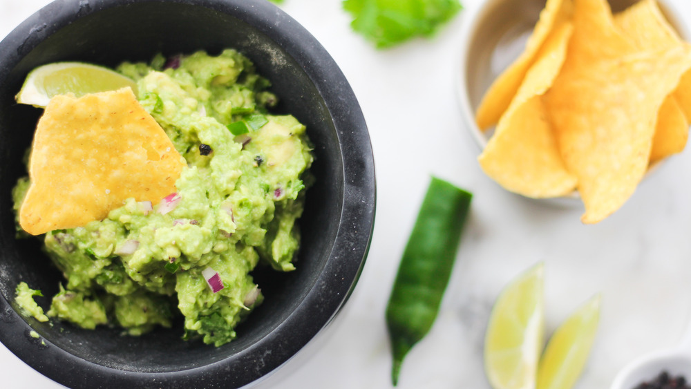 guacamole in black bowl on stone cutting board with tortilla chips