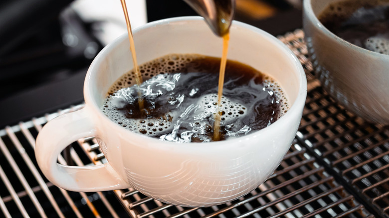 Coffee pouring into white mug on grate.