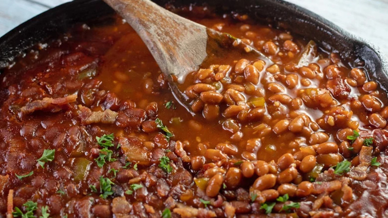 Baked beans in cast iron skillet with a wooden spoon