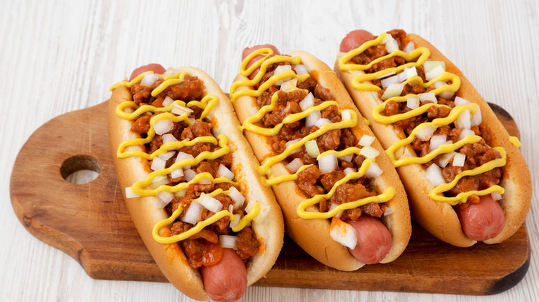 Three hot dogs loaded with chili and mustard on a cutting board