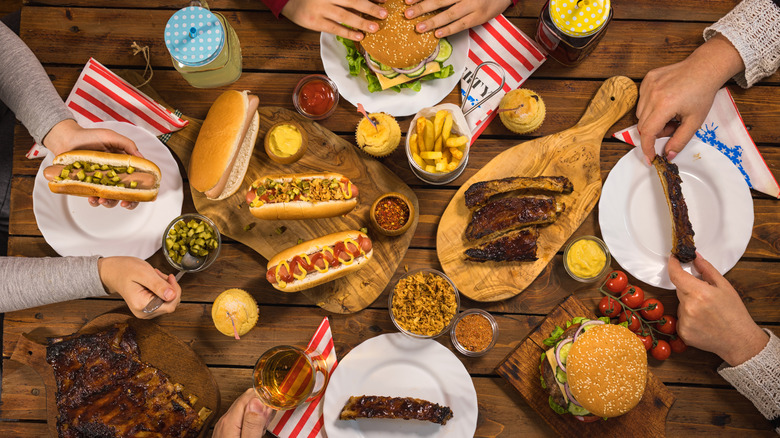 People eating hot dogs, ribs, burgers, and fries at a picnic table