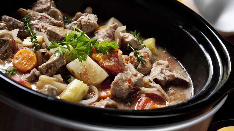 Beef chunks and ingredients in a black slow cooker. 