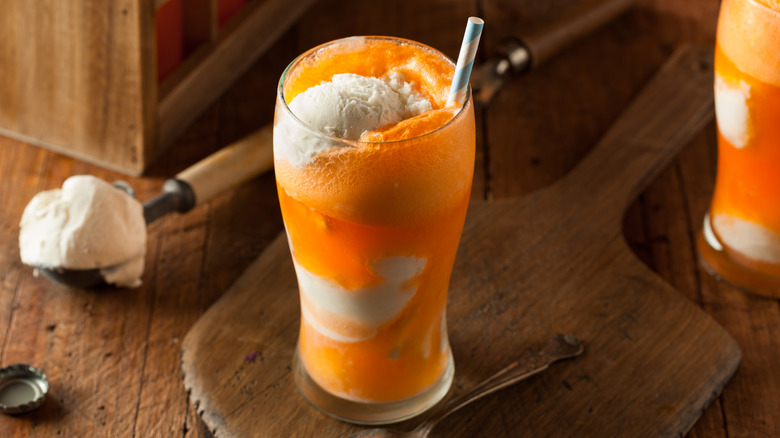 Orange soda and vanilla ice cream creamsicle ice cream float with paper straw and an ice cream scoop