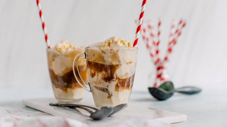 Two glasses of homemade root beer floats with red and white paper straws and dessert spoons