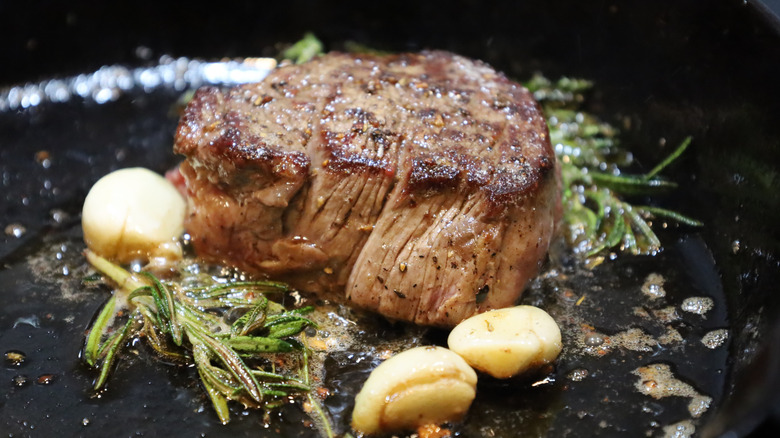 Steak in frying pan with garlic cloves and rosemary
