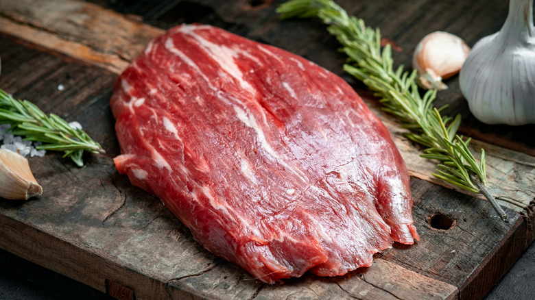 Raw flank steak with rosemary sprigs on cutting board