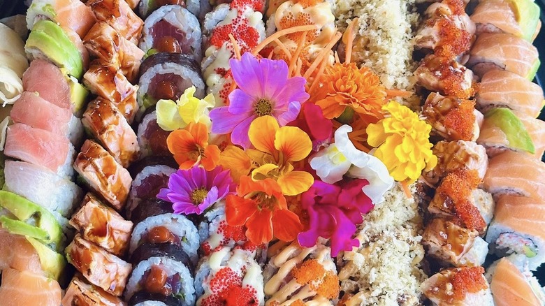 sushi board with assorted rolls and decorative flowers at the center