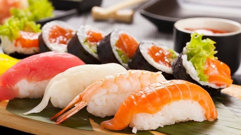 Tray with maki roll on the back and 4 different types of nigiri on the front: red salmon, white salmon, pink salmon, and shrimp.