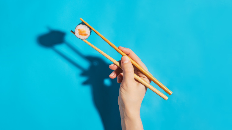 Hand holding sushi between two chopsticks