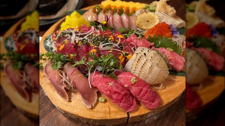 Assorted niguiri and sashimi on a tray, made with several types of salmon, along cubed fruits, caviar and a slice of lemon