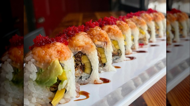 Vegetarian sushi roll with avocado, with a red sauce on top.