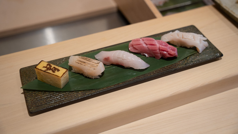 Five types of nigiri on top of a decorative leaf