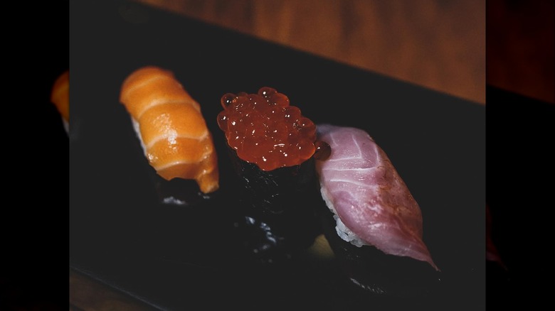 A red salmon nigiri, maki topped with red caviar, and another nigiri.