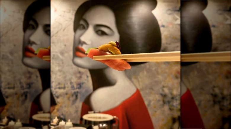 Chopsticks holding a piece of raw fish sushi