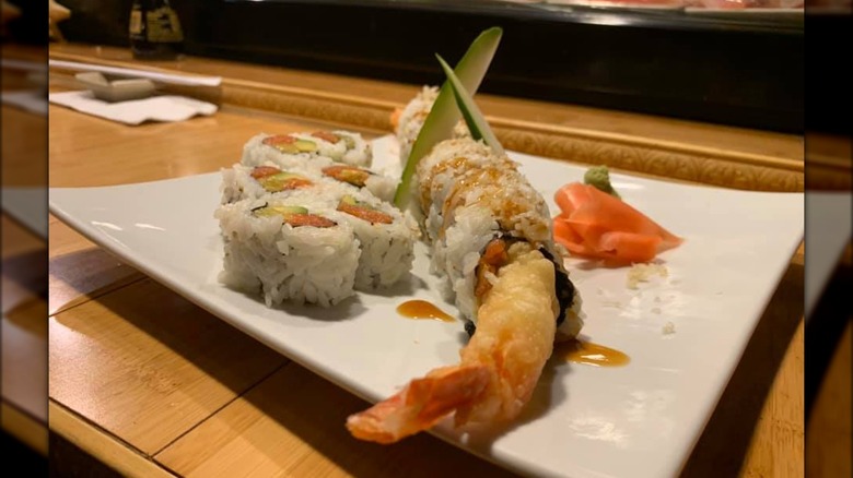 2 types of sushi rolls on a white plate. One with salmon and avocado, the other one with a shrimp tail sticking out of it.