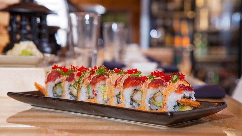 Sushi rolls made with tempura shrimp, spicy tuna, avocado, tuna, tobiko, negi, and sweet chili aioli on a tray