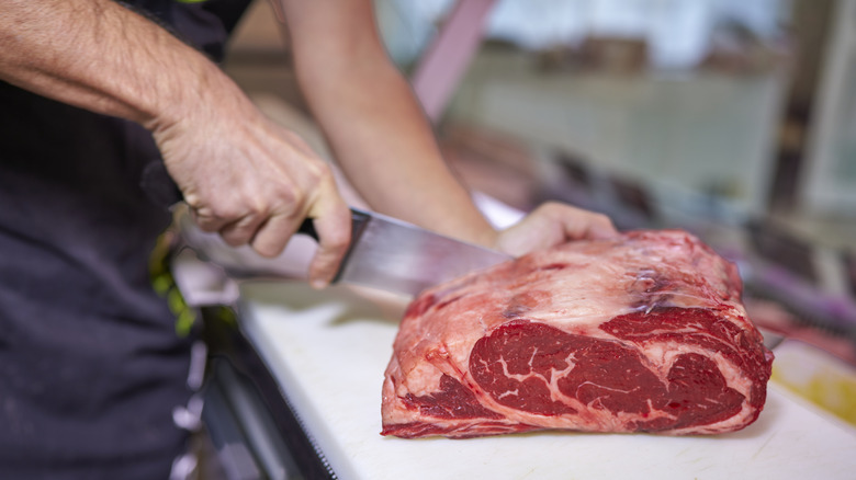 Hands of a butcher cutting sirloin steak with his knife