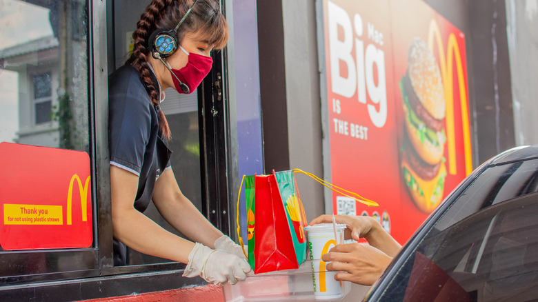 A McDonald's employee handing food to a customer at the drive-thru.