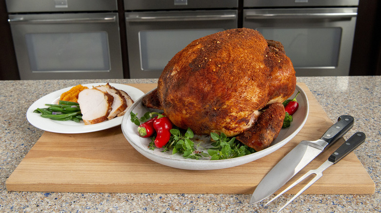 A roast turkey on wood block next to knives
