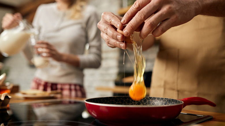 Person cracking egg into frying pan